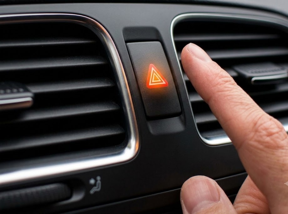 Diagram contrasting turn indicators (one side flashing amber = turn or lane change) with hazard/emergency warning lights (all four corners flashing simultaneously), plus three small scenario icons: breakdown, immobilised vehicle, and roadside assistance