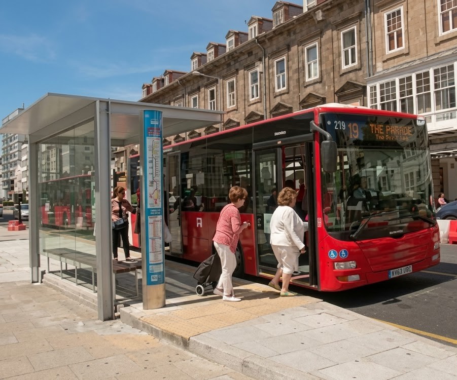 Illustration of a bus stopped at a stop with a passenger stepping down between the bus and the pavement while a car approaches and must yield