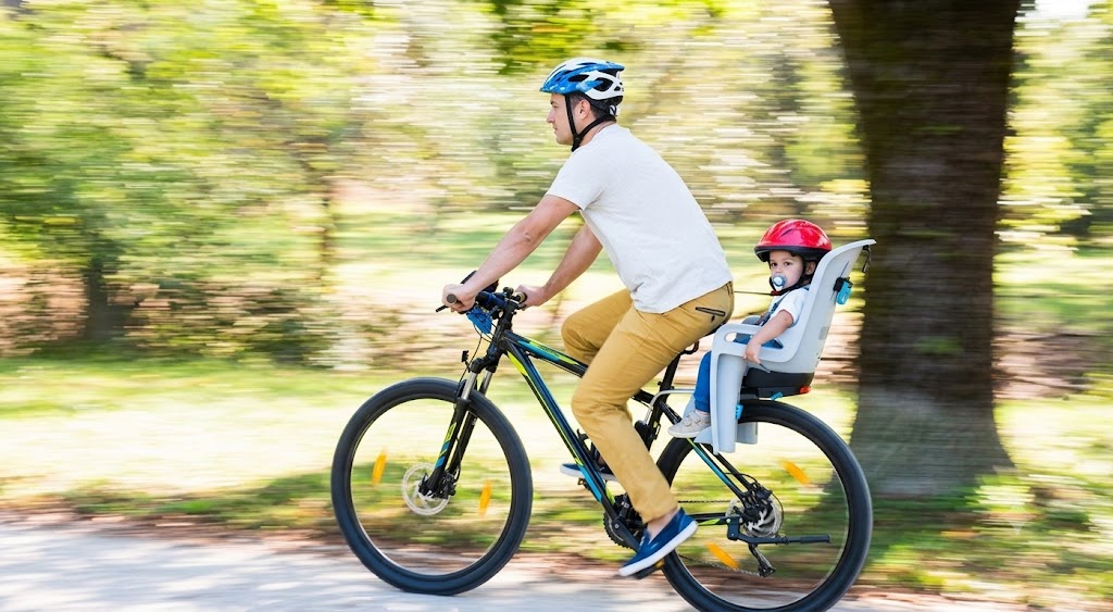 Illustration of an adult cyclist with a child (up to 7 years old) secured in an approved rear-mounted child seat on a bicycle