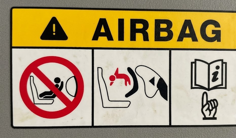 Diagram of a car interior showing a rear-facing child seat placed in the front passenger seat with the airbag deactivation indicator illuminated on the dashboard
